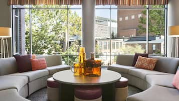 Un área de descanso moderna con una mesa redonda, dos sofás y vistas a edificios a través de grandes ventanales.