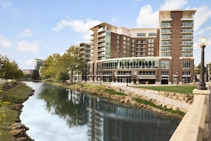 A multi-story hotel with a river in front, featuring a modern design with glass and brick facades. - Embassy Suites by Hilton Greenville Downtown Riverplace (Greenville)