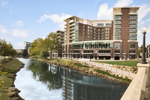Un hotel de varios pisos con un río frente a él, que presenta un diseño moderno con fachadas de vidrio y ladrillo.