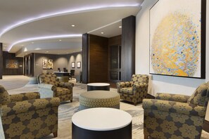 A modern lobby with seating areas, a reception desk, and a large abstract painting. - Embassy Suites by Hilton Greenville Downtown Riverplace (Greenville)