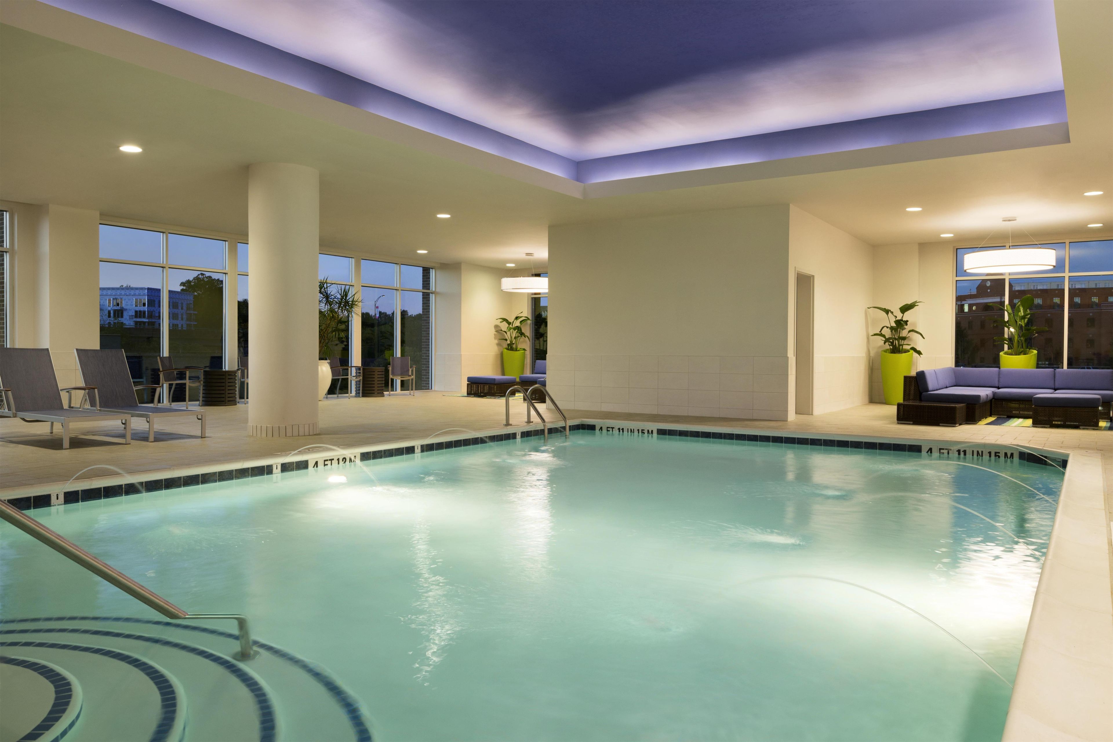 An indoor swimming pool with clear water, surrounded by lounge chairs and potted plants.