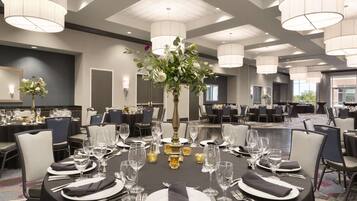 A banquet hall with round tables set for dining, featuring white tablecloths, black napkins, and clear glassware.