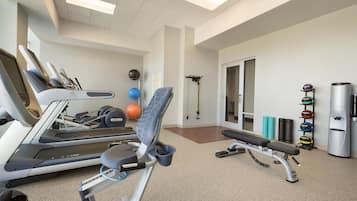 A fitness room with exercise equipment, including a treadmill, elliptical, and weights.