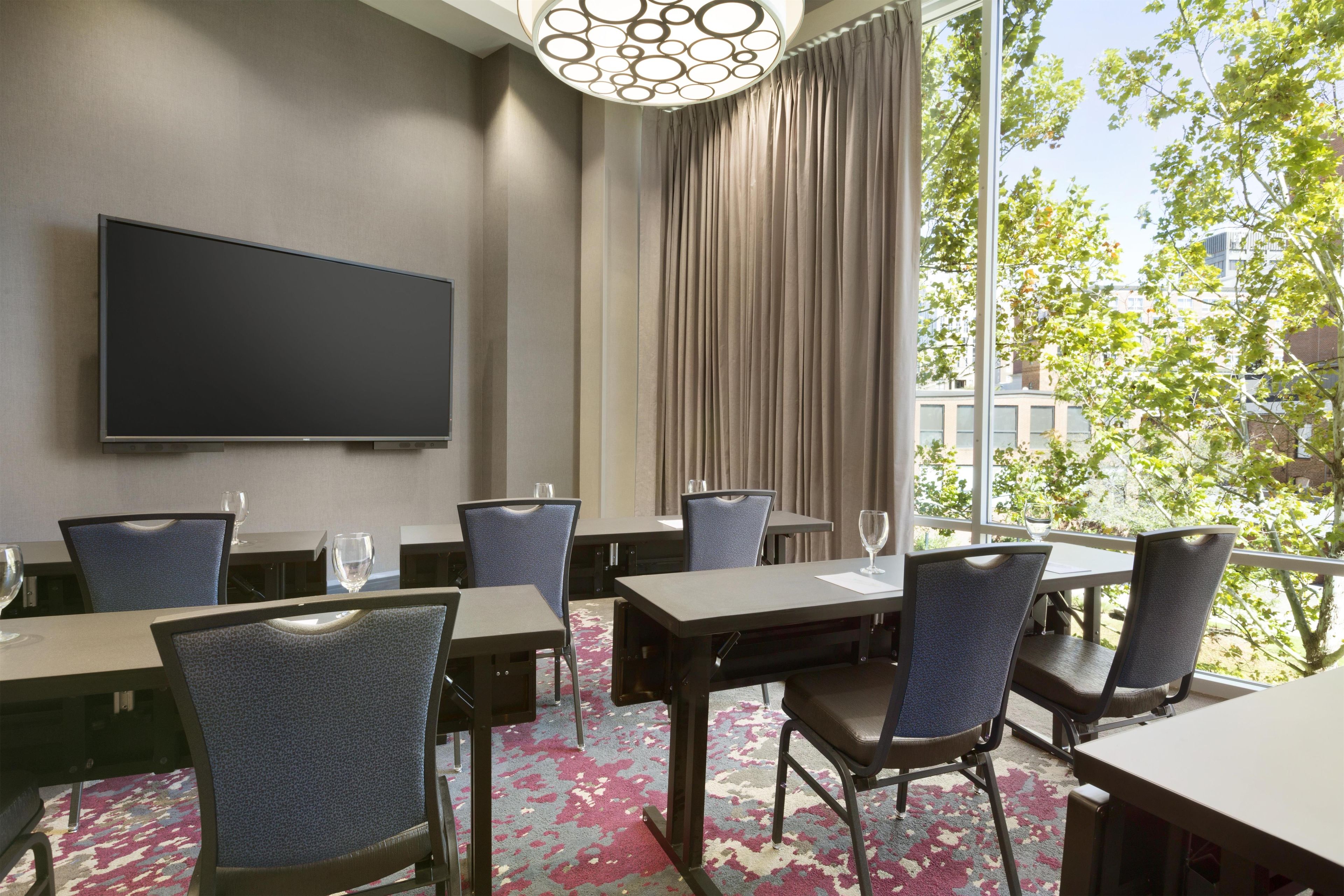 A hotel conference room with a large flat-screen TV, multiple tables, and chairs.