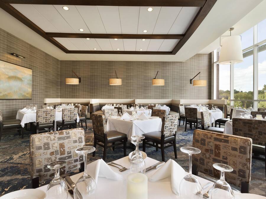 A dining area with tables set for service, patterned chairs, and pendant lighting.