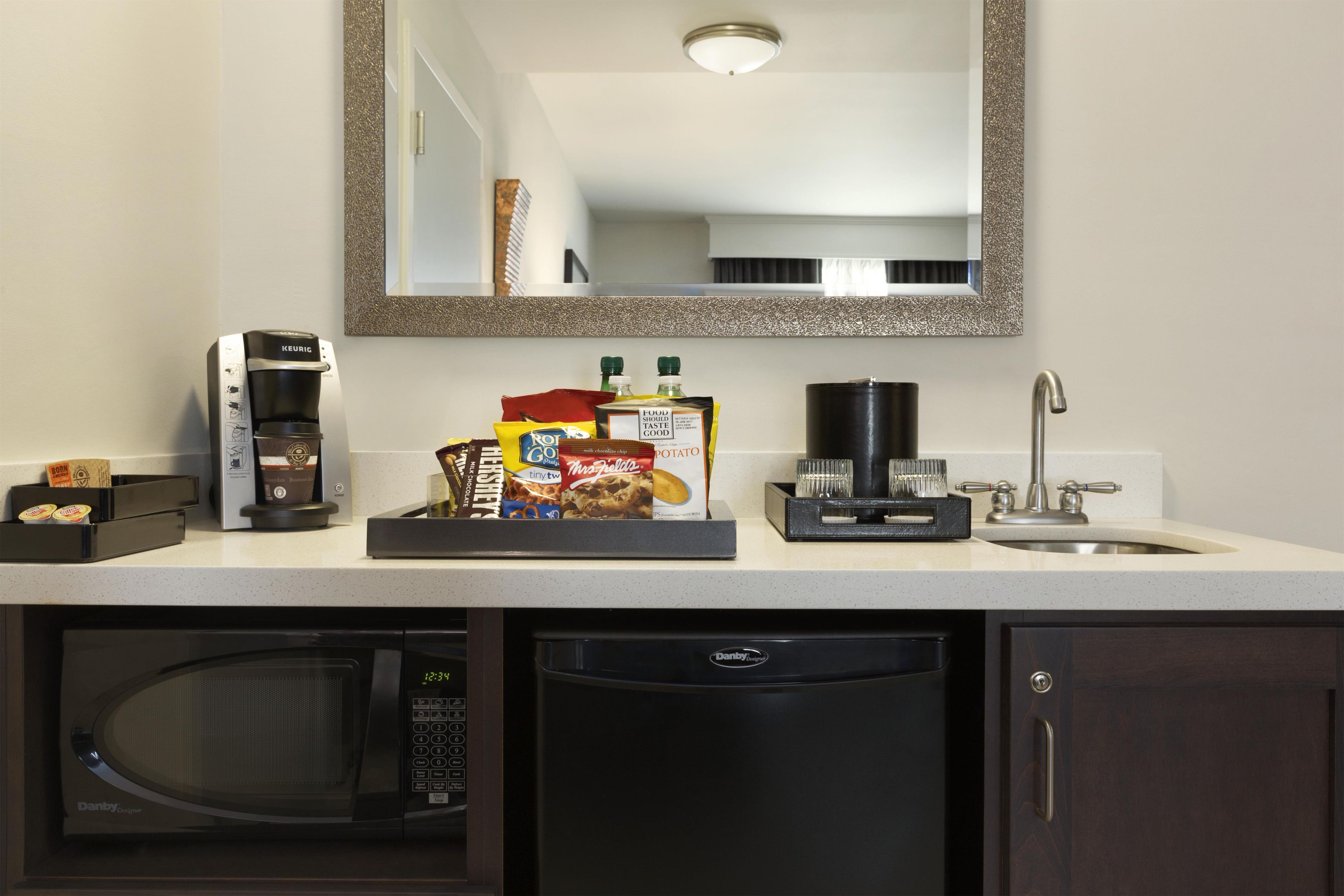 A kitchenette with a coffee maker, microwave, and a tray of snacks.