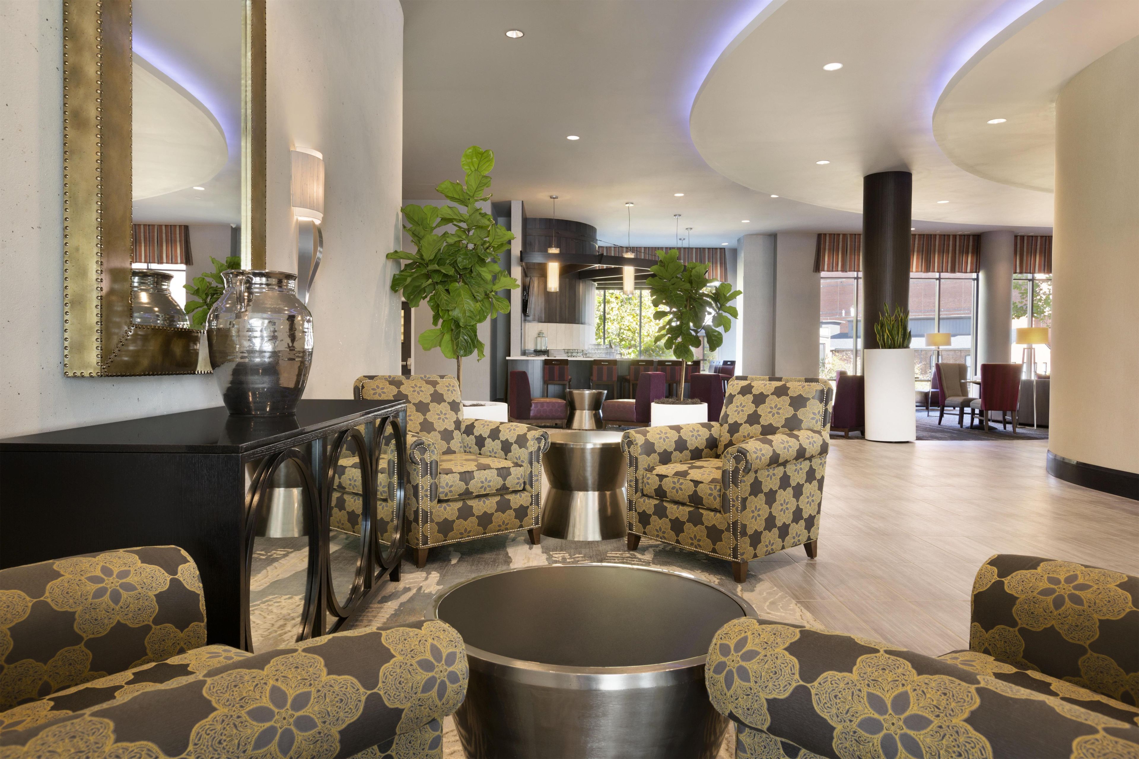 A spacious lobby with a round coffee table, two armchairs, a sofa, and a large mirror.