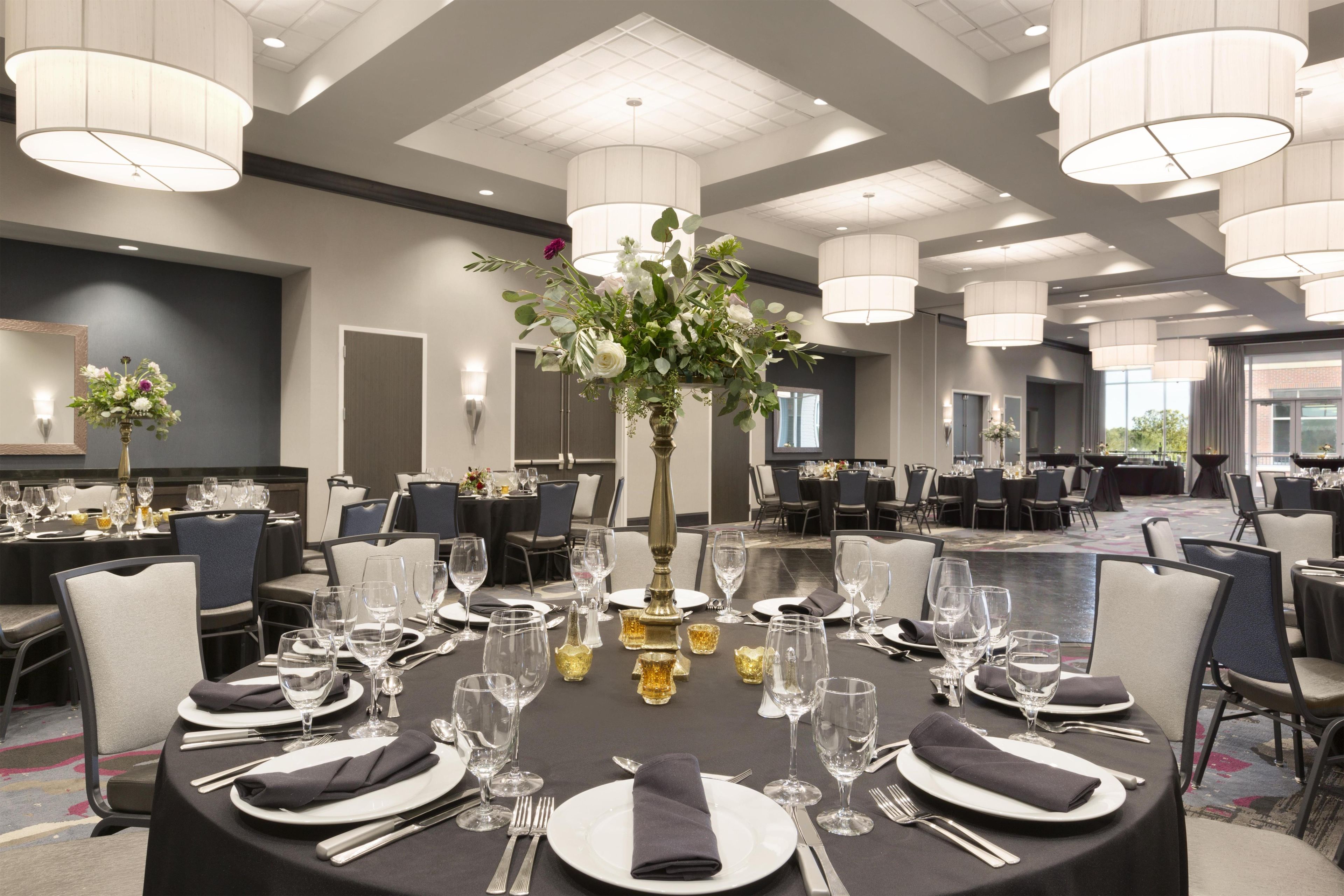 A banquet hall with round tables set for dining, featuring white tablecloths, silverware, and clear glassware.