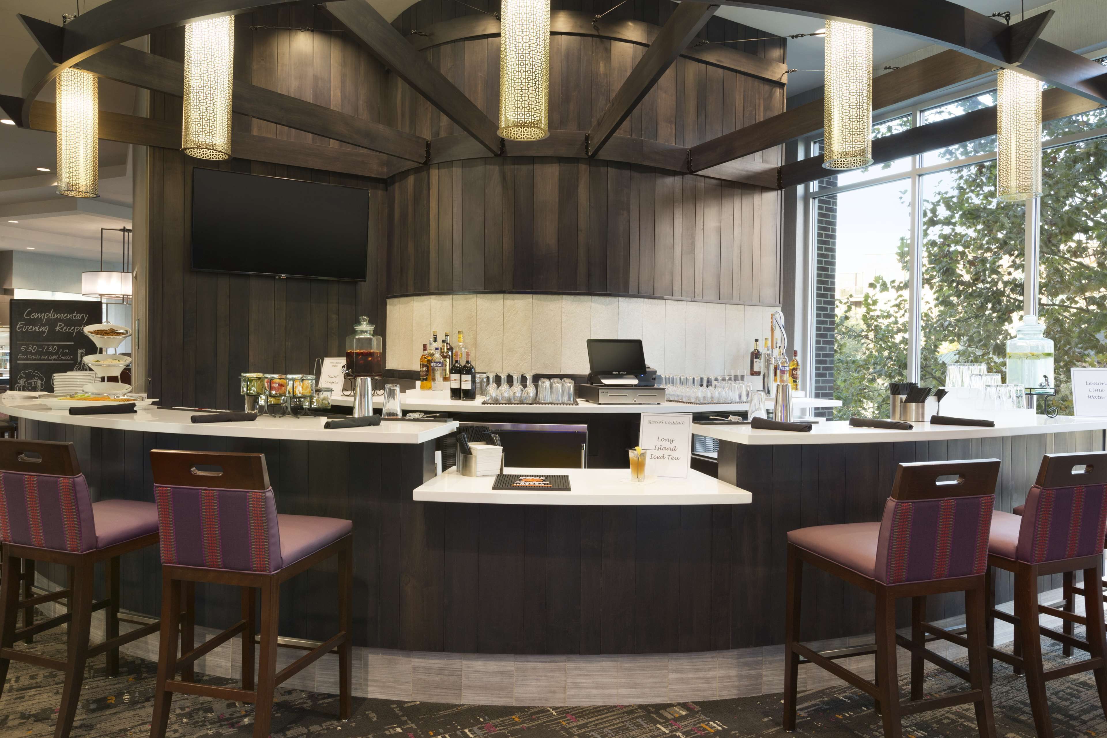 A bar area with a curved counter, bar stools, and a television screen.