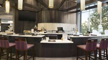 A bar area with a curved counter, bar stools, and a television screen.