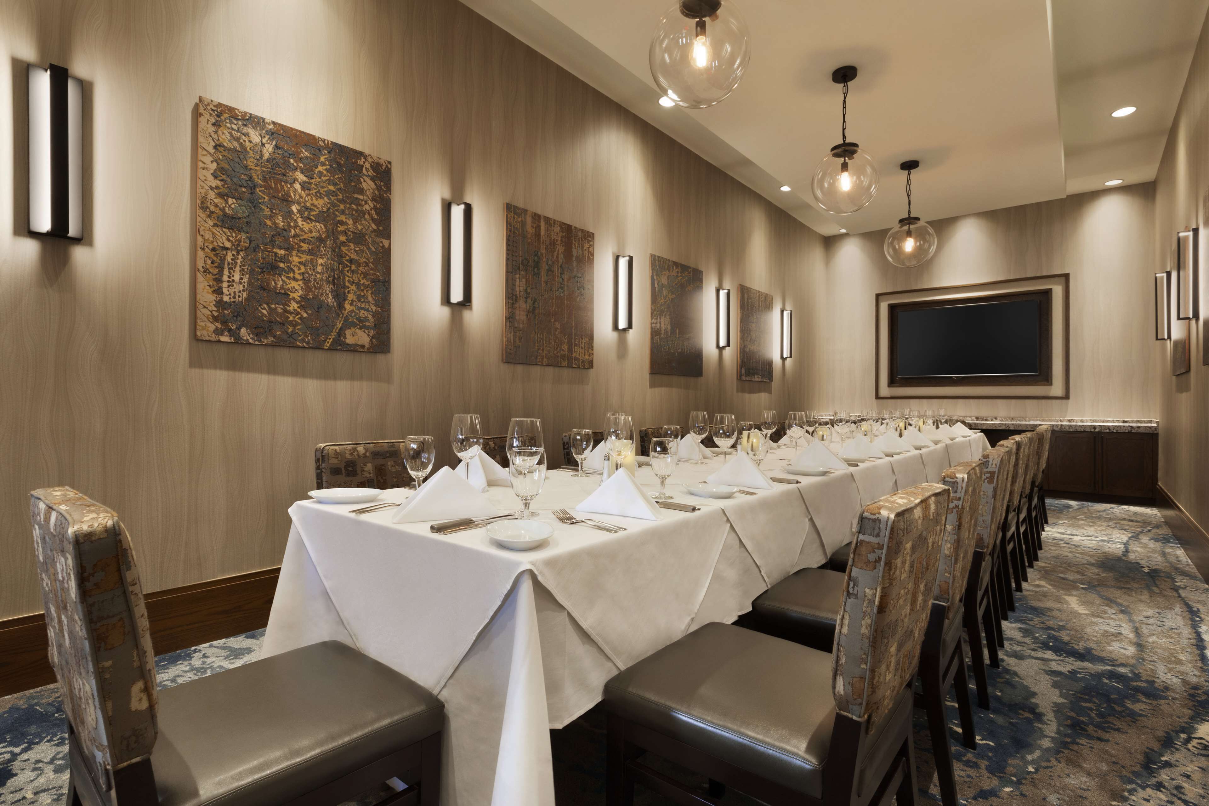 Une salle de conférence dotée d’une longue table préparée pour une réunion, avec des chaises et des tables, un grand écran et un éclairage d’ambiance.