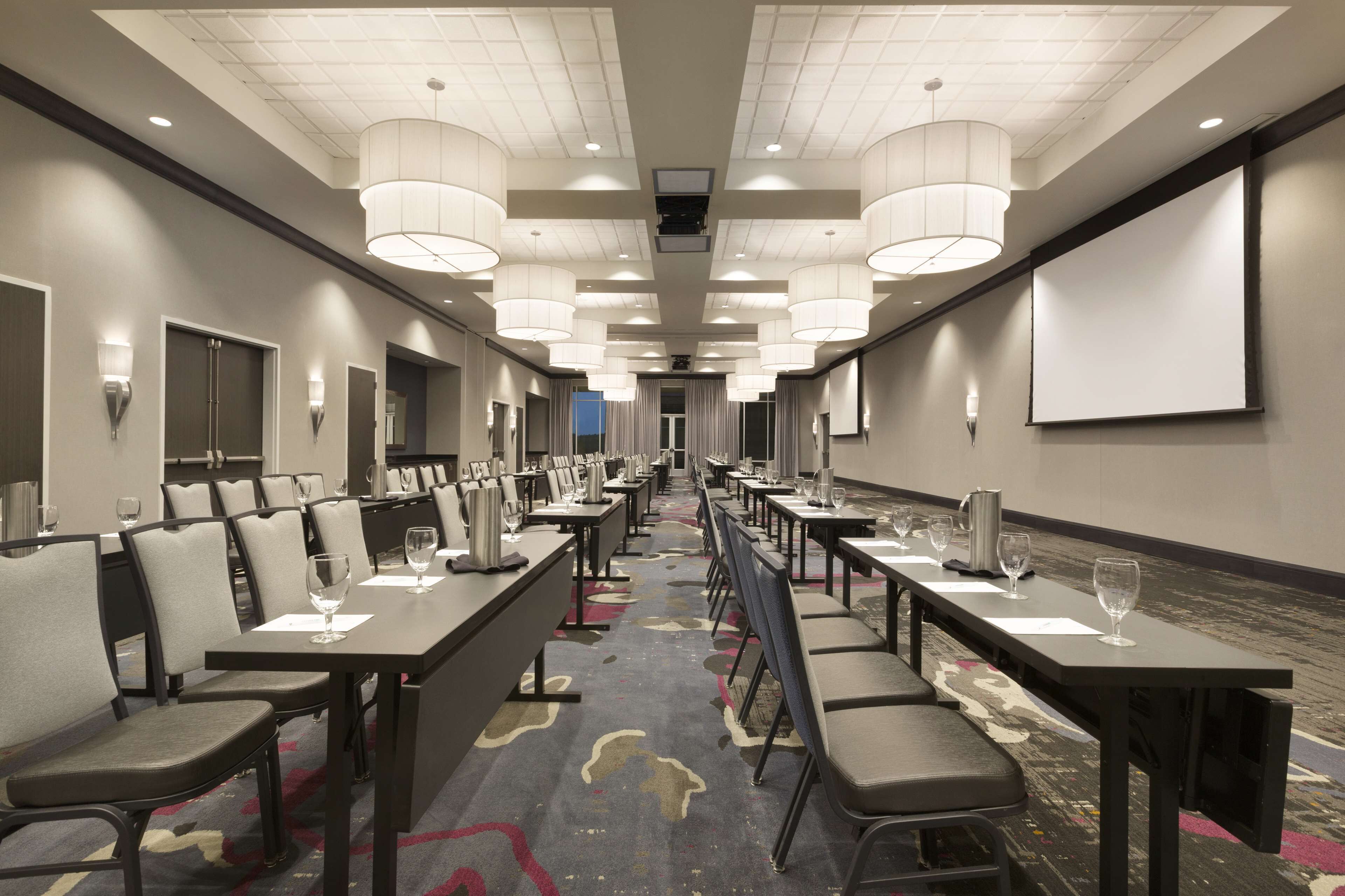 A conference room with long tables, chairs, and a projector screen.