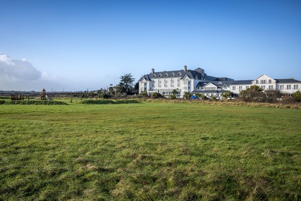 A large, multi-story building with a symmetrical facade, a well-maintained lawn in the foreground, and a clear sky. - Garryvoe Beach Homes (Garryvoe)