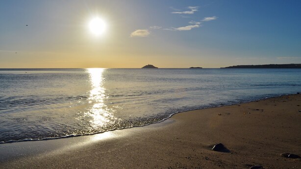 A beach with calm waters reflecting the sun, a clear sky, and distant landforms. - Garryvoe Beach Homes (Garryvoe)