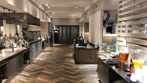 A modern hotel lobby with a herringbone wood floor, a reception desk, and a buffet area with food and drinks. - Embassy Suites by Hilton McAllen Convention Center (McAllen)