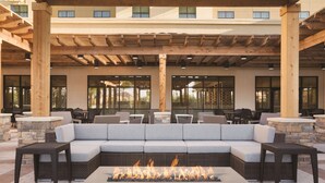 A covered outdoor seating area with a fire feature, stone walls, and a view of the building in the background. - Embassy Suites by Hilton McAllen Convention Center (McAllen)
