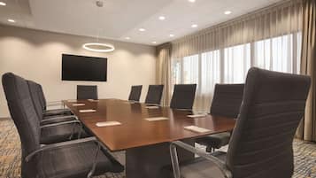 Un salón de conferencias con una gran mesa, seis sillas, un televisor de pantalla plana y un accesorio de iluminación en el techo.