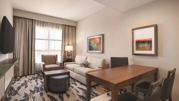 A hotel room with a sofa, a dining table, a TV, and artwork on the walls.