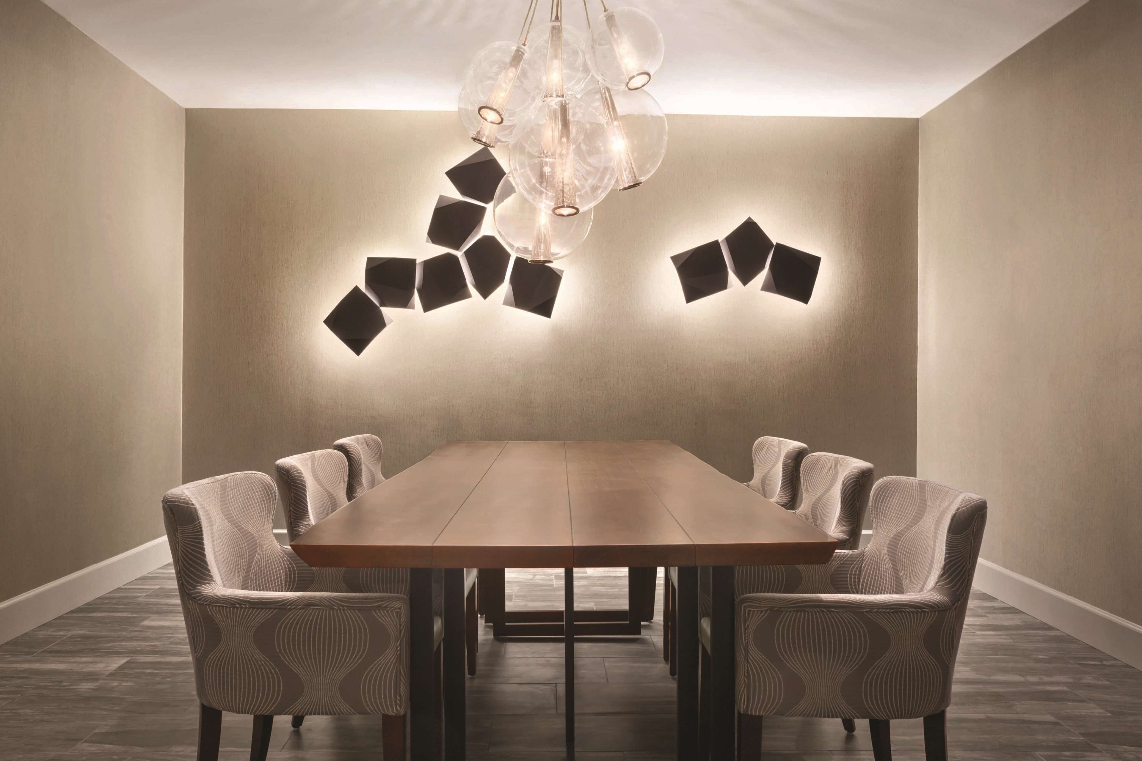 Een vergaderruimte met een lange tafel, zes stoelen en een moderne kroonluchter.