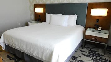Una habitación de hotel con una cama grande, dos mesitas de noche con lámparas, una mesita con un teléfono y una alfombra estampada.