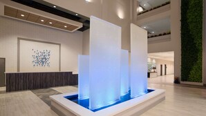 A modern lobby with a water feature, a reception desk, and a green wall. - Embassy Suites by Hilton McAllen Convention Center (McAllen)