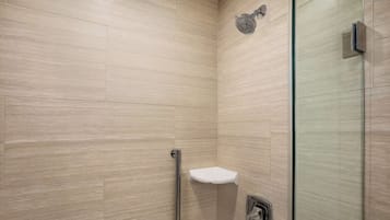 Une salle de bain moderne avec des carreaux de couleur beige, une douche en verre, un lavabo blanc avec un robinet chromé et une barre d’appui.