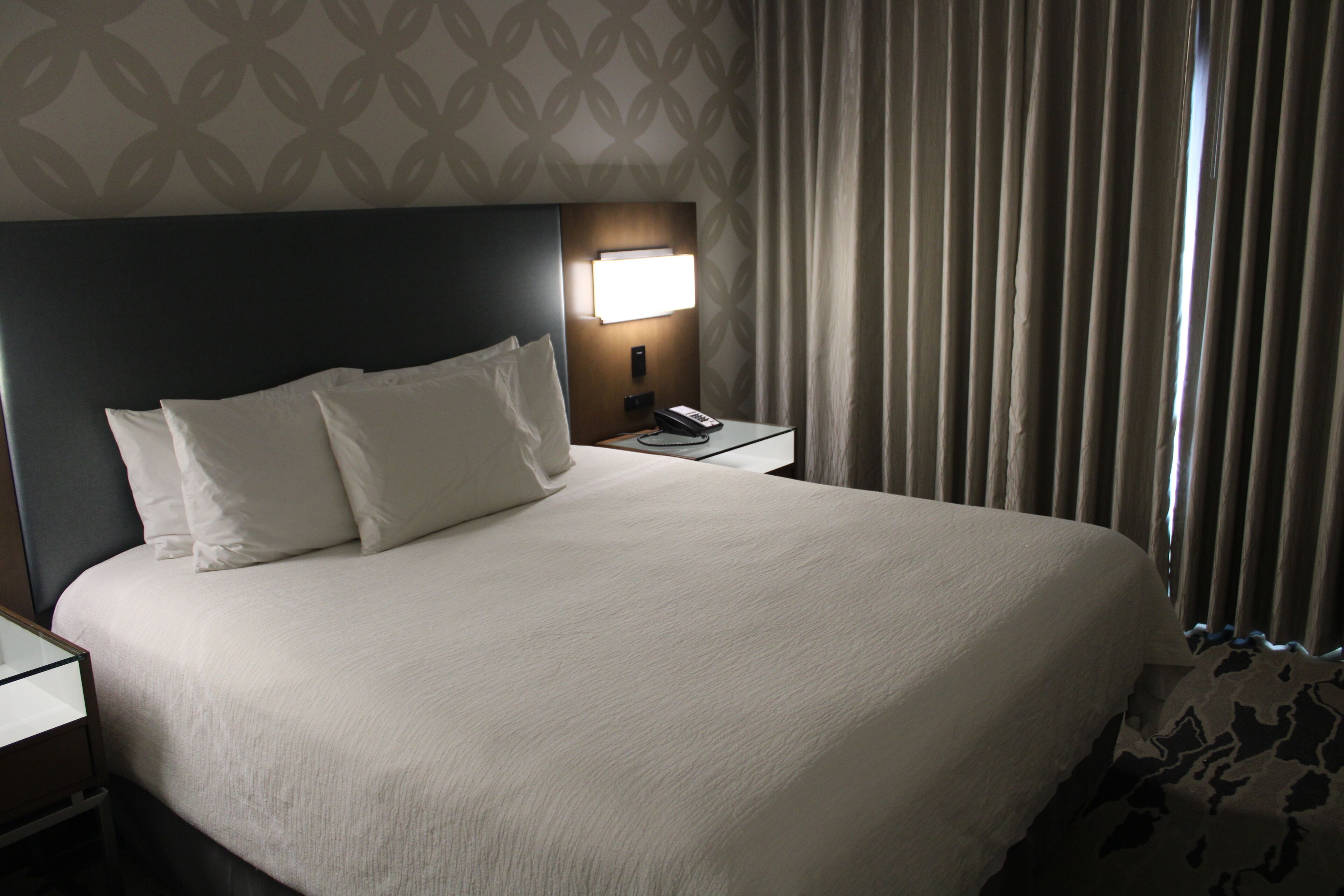 Una habitación de hotel con una cama grande, una mesita de noche con lámpara y un papel tapiz estampado.