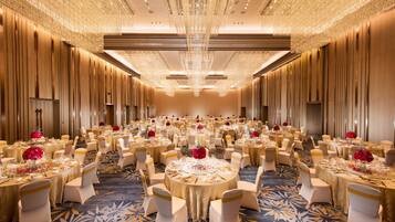 A banquet hall with round tables, white chairs, and red floral centerpieces.