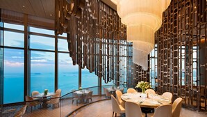A modern dining area with a panoramic ocean view, featuring a round table set for six, elegant chairs, and a decorative metal partition. - Conrad Xiamen (Xiamen)