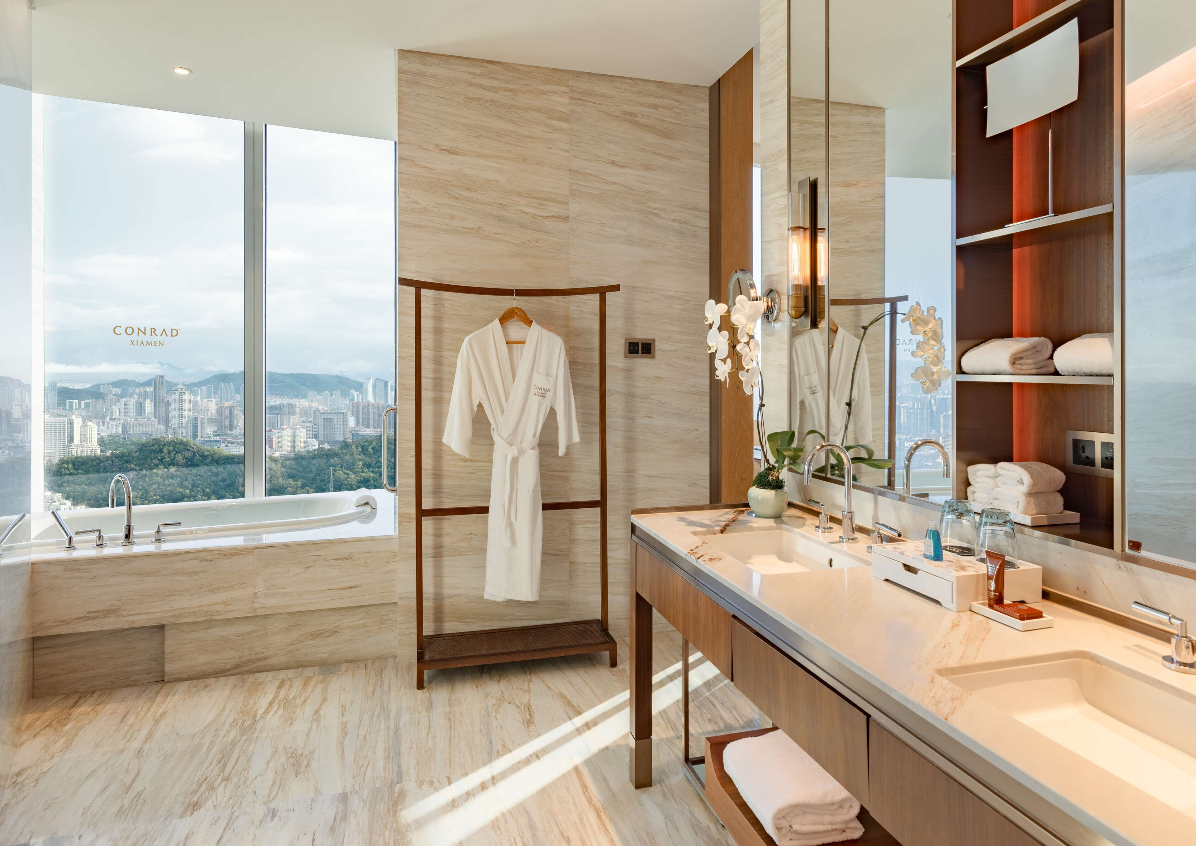A modern bathroom with a large window, a bathtub, a vanity with a mirror, and a robe rack.