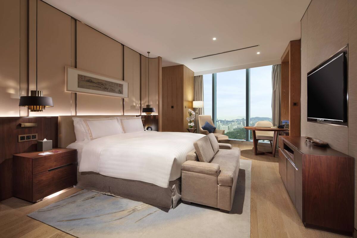 A modern hotel room with a large bed, a sofa, a desk, and a TV.