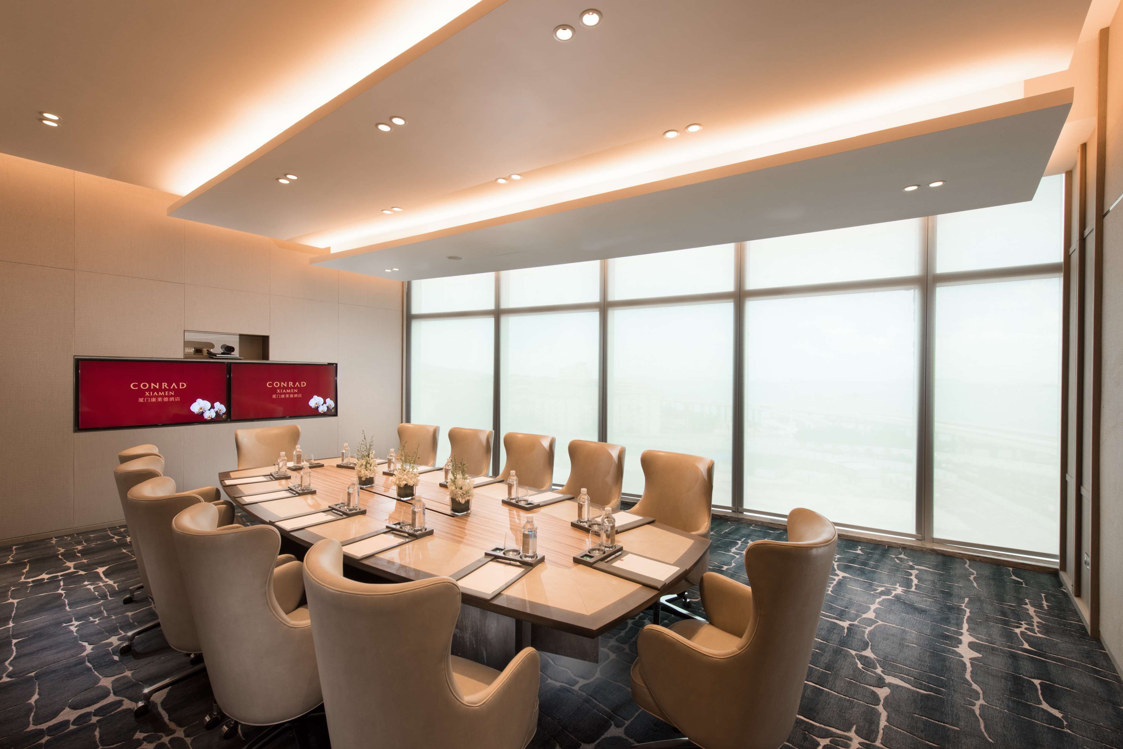 A conference room with a long table, multiple chairs, and a large window with a view.