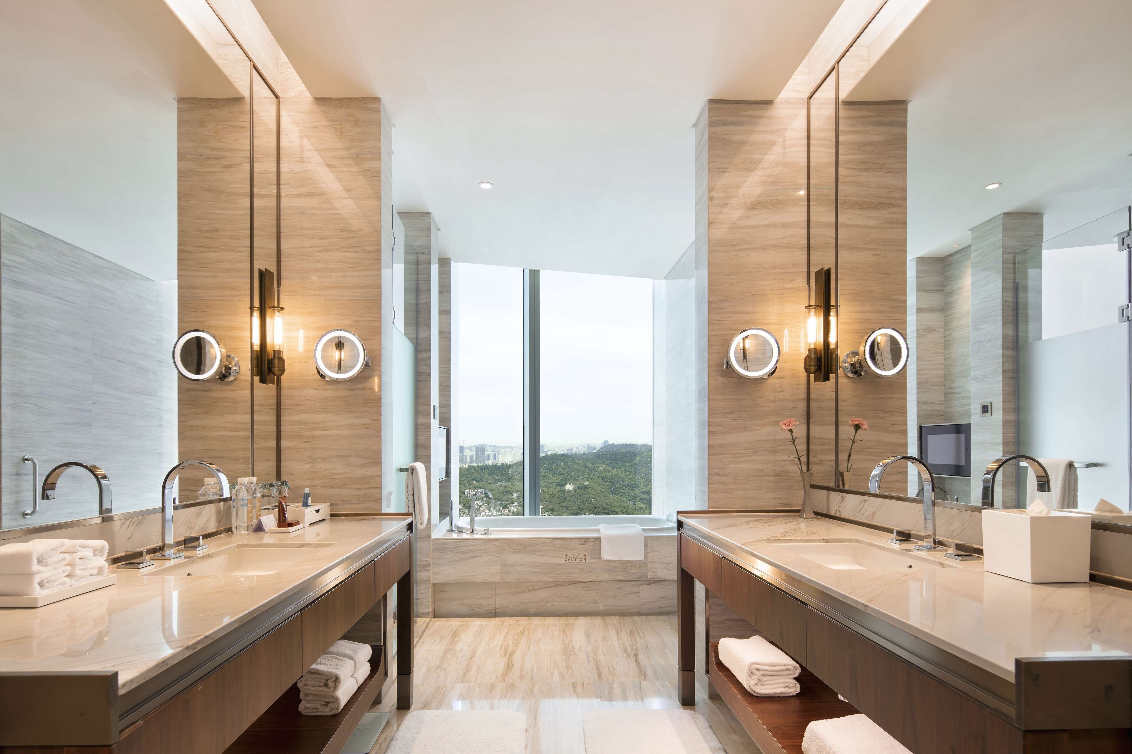 A modern bathroom with dual sinks, large mirrors, and a view of a cityscape.