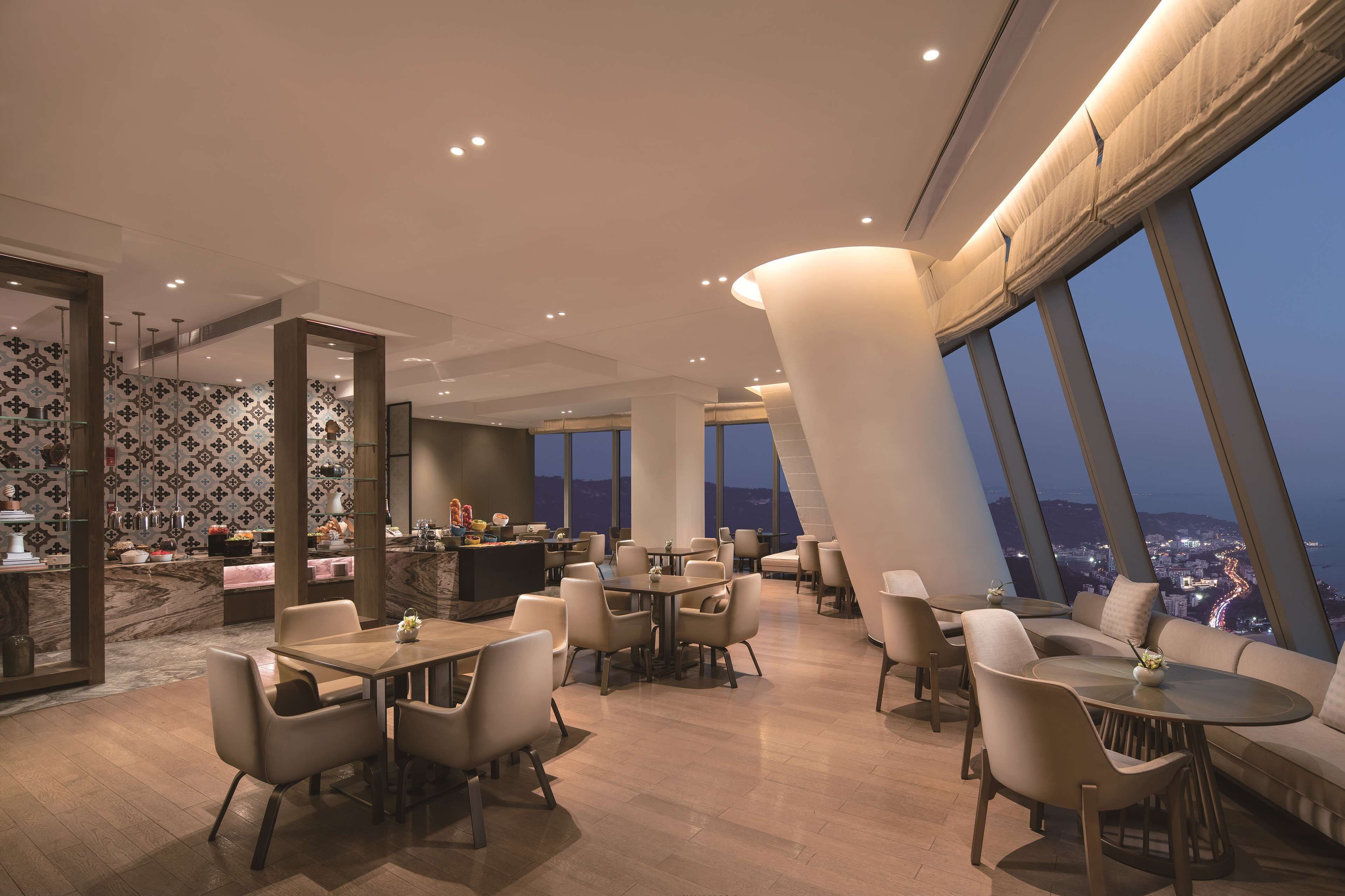 A modern dining area with tables and chairs, a bar area, and large windows offering a city view.