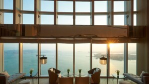 A spacious living area with a large window overlooking a body of water, featuring modern furniture and a floor lamp. - Conrad Xiamen (Xiamen)