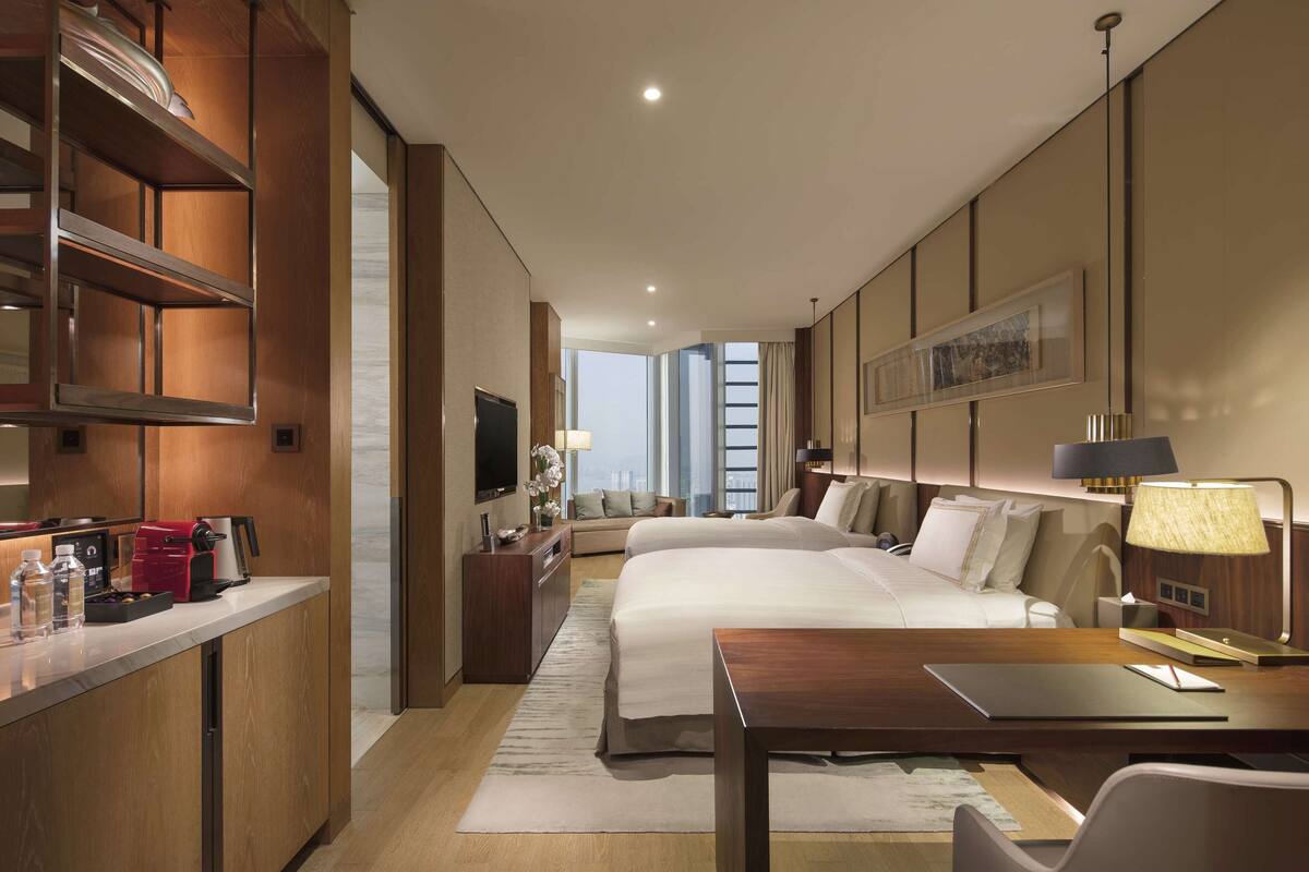 A hotel room with a large bed, a desk, a sofa, a TV, and a view of the city.