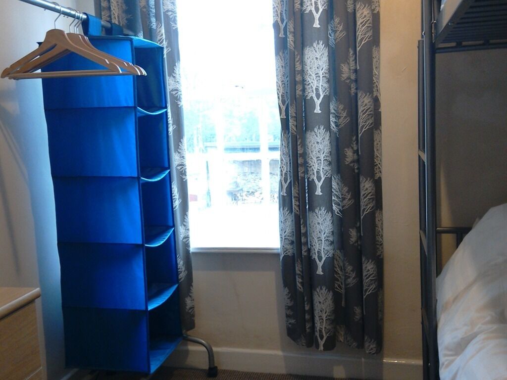 Une chambre avec un lit superposé, un meuble de rangement bleu, un porte-manteau en bois et des rideaux à motifs.