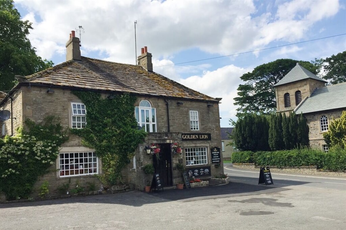 A stone building named 'Golden Lion' with ivy, a signboard, and a small garden area.