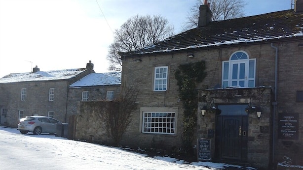 A stone building with a black door, a window with a grid pattern, and a signboard.