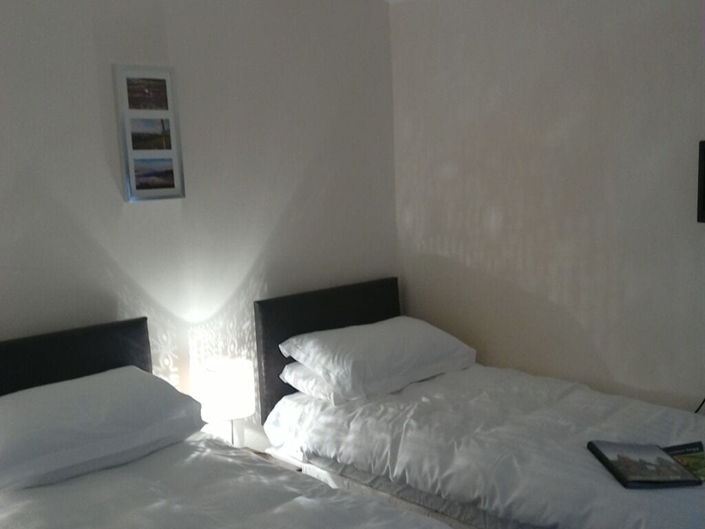 A simple, unadorned hotel room with a single bed, a nightstand, and a small picture frame on the wall.