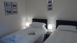 A hotel room with two beds, each with a nightstand and a lamp. There are framed pictures on the wall.