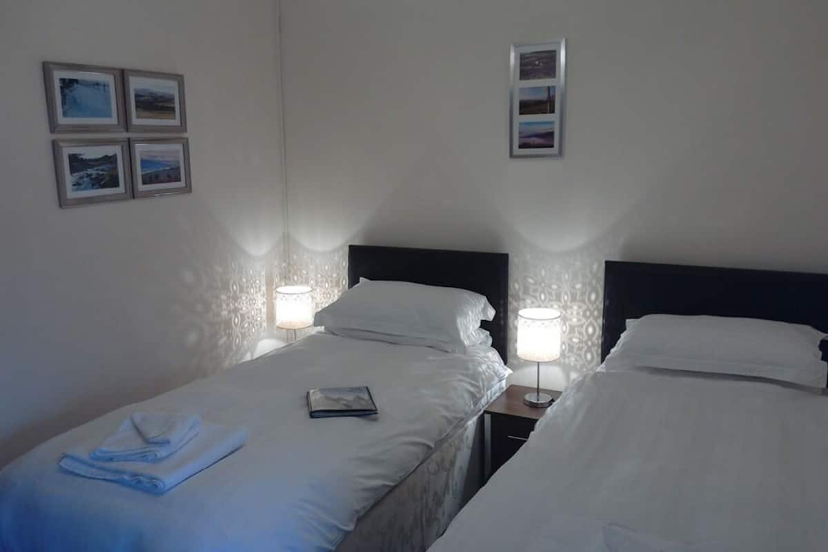 A hotel room with two beds, each with a nightstand and a lamp. There are framed pictures on the wall.