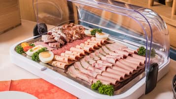 Een buffet met diverse vleessoorten, waaronder plakjes ham en worstjes, uitgestald op een schaal.