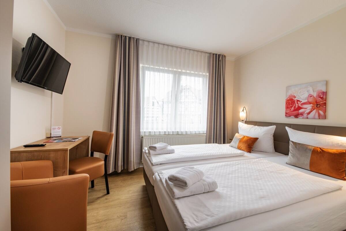 A hotel room with two beds, a desk, a TV, and a painting.