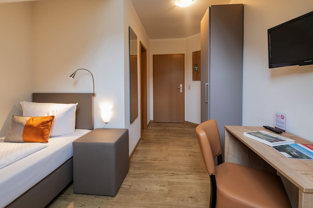 A hotel room with a bed, a desk, a chair, a TV, and a door.