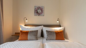 A double bed with white and orange bedding, two bedside lamps, and a floral artwork on the wall. - Hotel Bamberger Hof (Wutha-Farnroda)