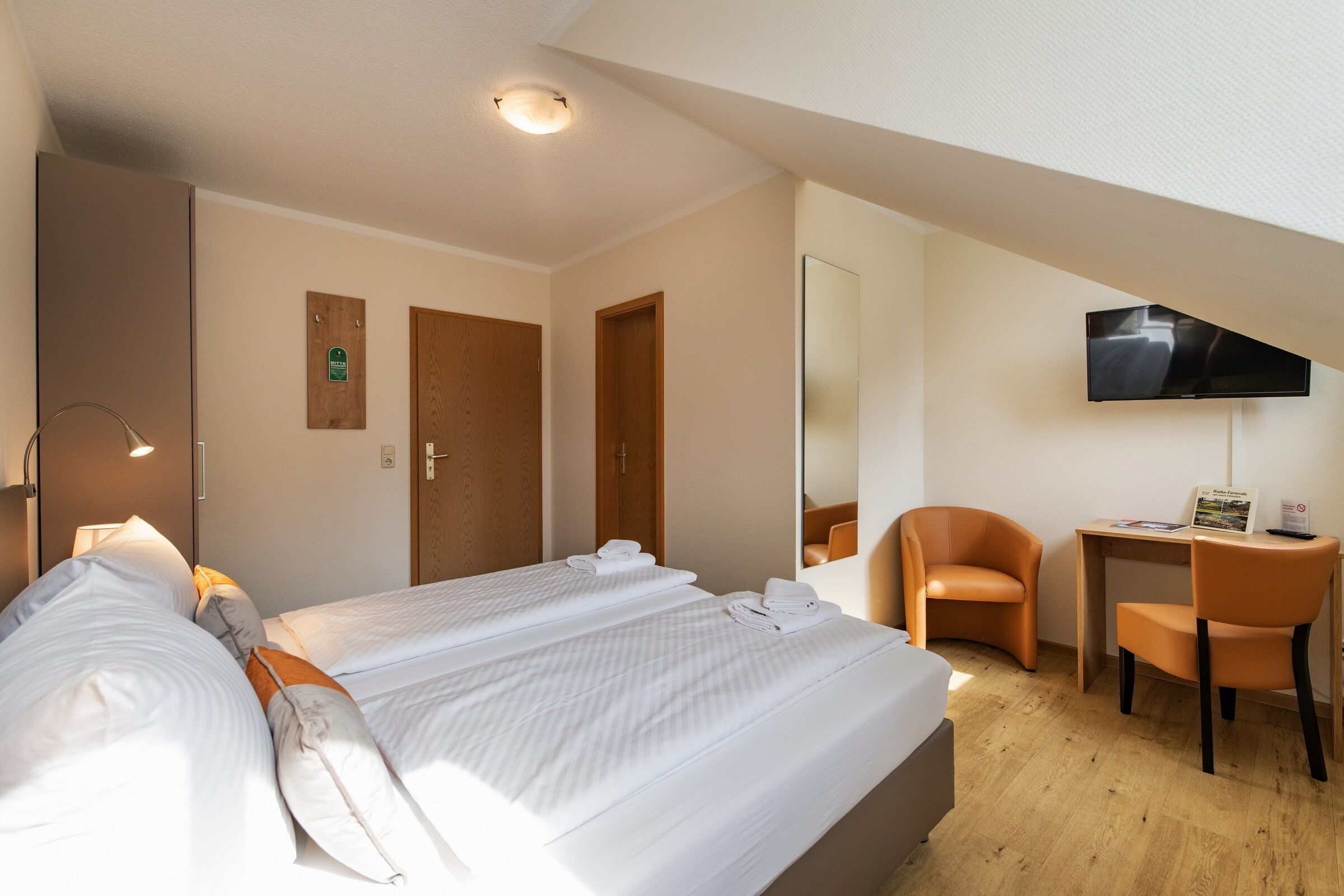 A hotel room with two beds, a desk, a chair, a TV, and a mirror.