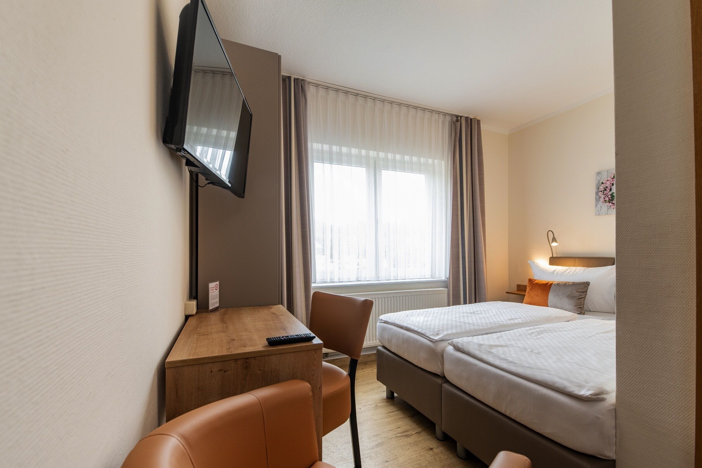 Een hotelkamer met een bed, bureau, stoel, televisie en raam met gordijnen.