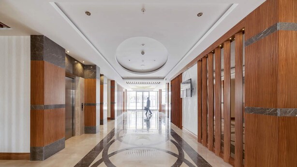 A modern hotel corridor with a polished marble floor, wooden paneling, and a central elevator. - Lamec Hotel Business (Gebze)