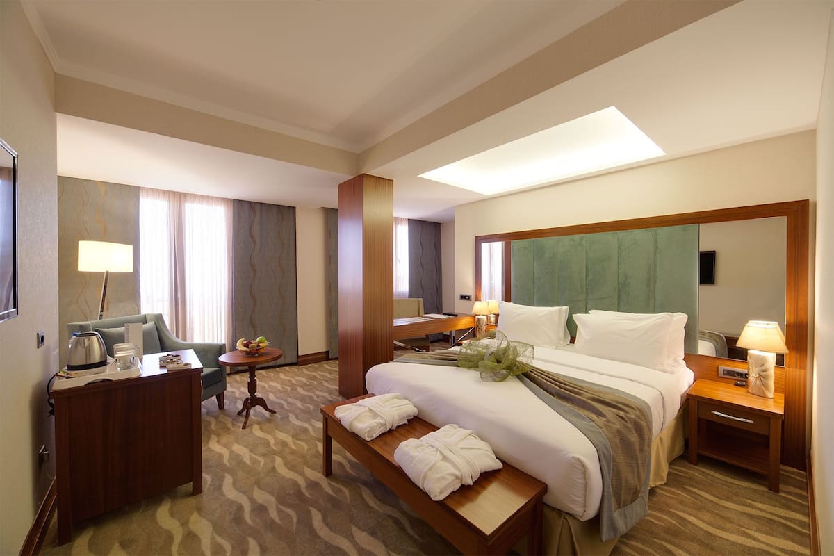 A hotel room with a large bed, bedside tables, a desk, a chair, and a small table with a lamp.